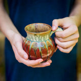 An 11 ounces small coffee mug in red and green held in two small hands, perfect as a gift for her for any occasion