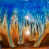 close up of a round pottery mug showing blue drips blending with brown glaze.