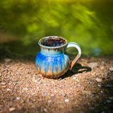 11 oz. ceramic small mug out in nature on the ground with a creek in the background