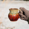  A handmade pottery mug in rustic red and green held outside in the snow