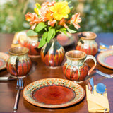 Green and red pottery tea cup as part of a spring outdoor table setting that includes lunch plates and a bud vase 