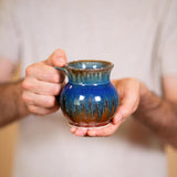 handmade small pottery coffee mug in blue and brown color held by two hands
